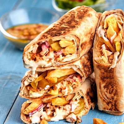 A chicken shawarma wrap cut in half, with fries, white sauce and pickles, in toasted flatbread