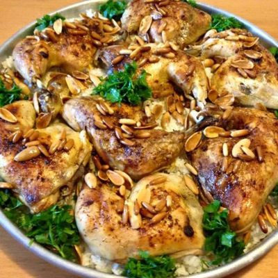 Pieces of browned chicken arranged over bread and rice, sprinkled with parsley and toasted almonds