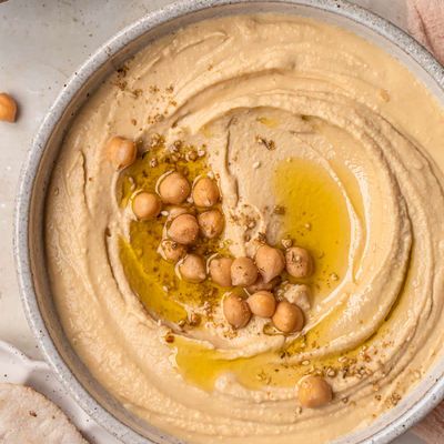 A bowl of hummus with whole chickpeas and olive oil pooled in the centre, served with slices of pita bread