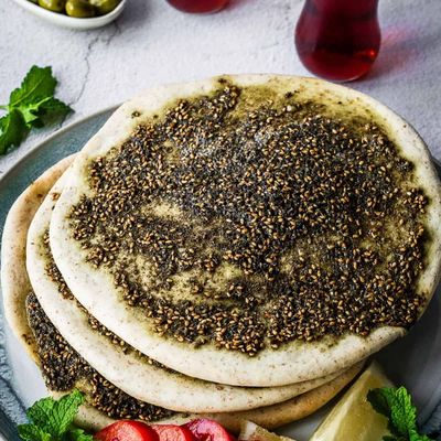 A stack of za'atar manakish with sesame, on a plate with slices of pink pickled vegetables, lemon and mint