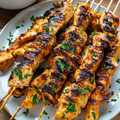 Grilled marinated chicken skewers, with flame marks and chopped parsley on top, on a white plate