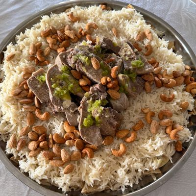 Slices of beef tongue arranged over rice with almonds and cashews, on a metal tray